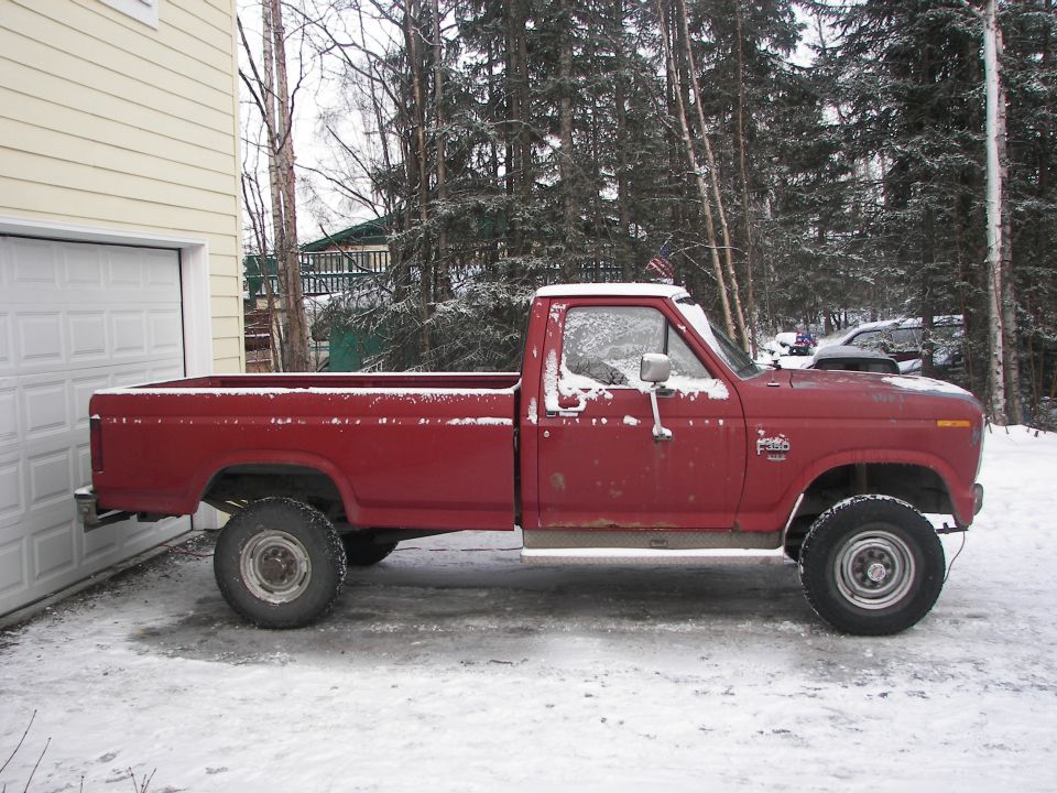 Red pickup truck with a white roof, parked in snow next to a garage