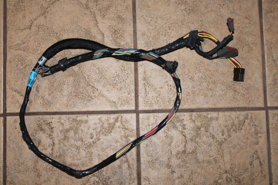 Automotive wiring harness with black conduit and multiple connectors on tile floor