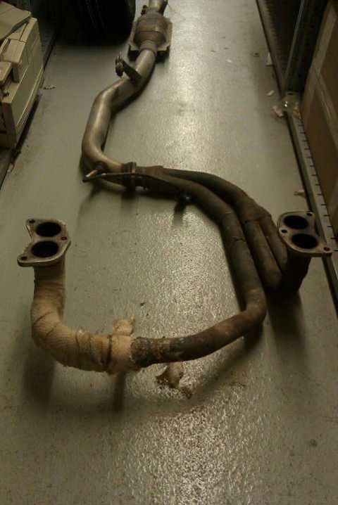 1998 Subaru Legacy - This is a vehicle exhaust system part, likely a manifold and catalytic converter, lying on a floor.