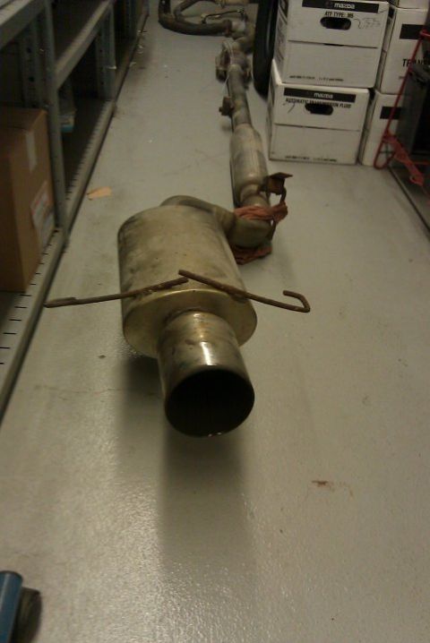 1998 Subaru Legacy - An exhaust system lies on the floor of a storage area, with boxes stacked nearby.