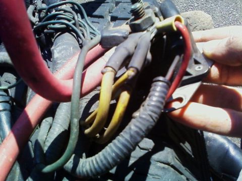 1990 Ford Bronco - Close-up of a starter relay (solenoid) area with a person's hand holding wiring, showing a large red battery cable, a yellow cable, and a c…