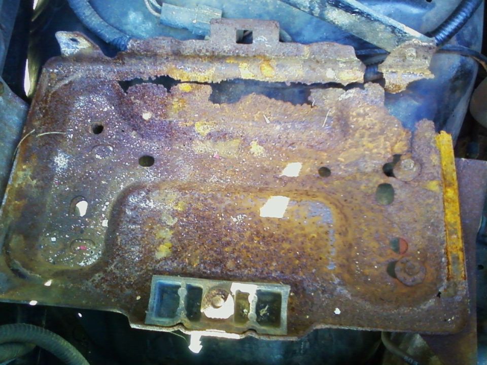 severely rusted metal battery tray with mounting holes and rubber isolators