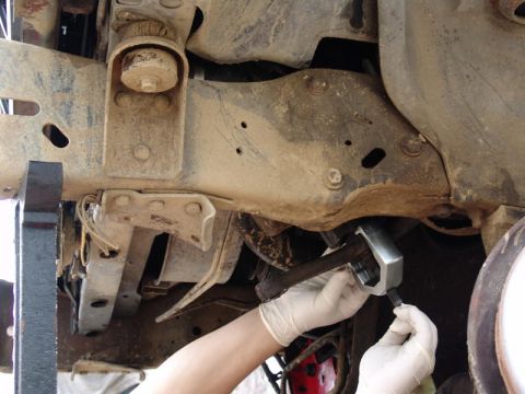 1982 Ford Bronco - Mechanic works on vehicle suspension system with specialized tool.