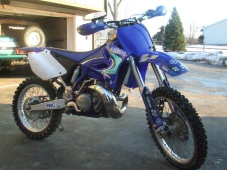 1996 Ford Bronco - A blue Yamaha dirt bike is parked outside a garage with a trailer visible in the background.