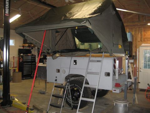 1996 Ford Bronco - A truck camper with a pop-up tent is shown in a garage setting, equipped with ladders and large off-road tires.