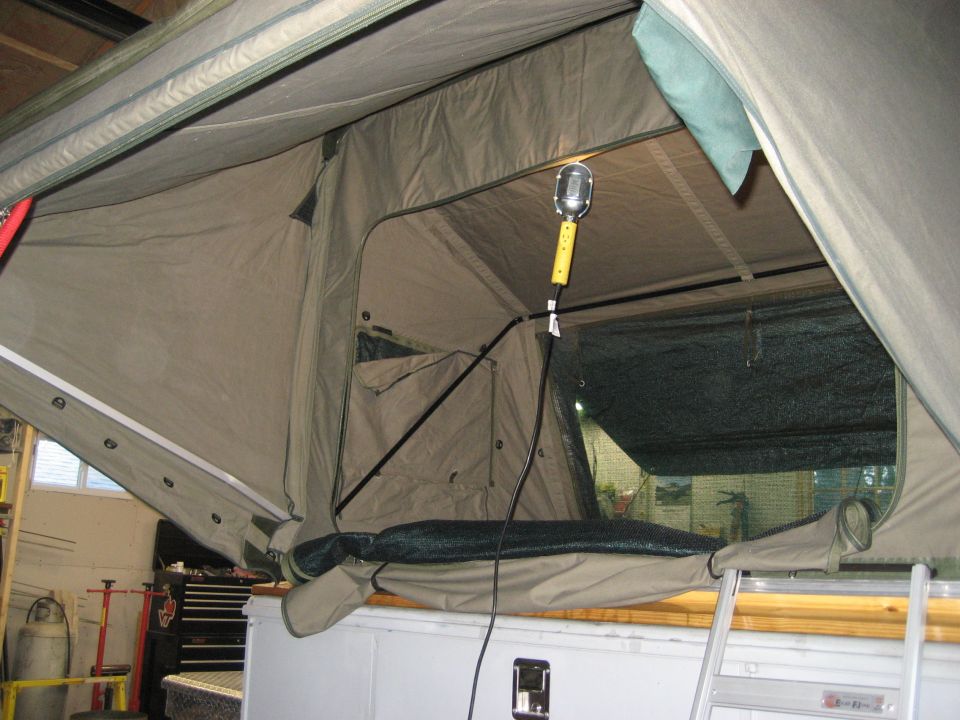 Interior of a tan pop-up camper tent with a hanging light fixture and a ladder visible