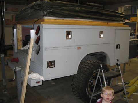 1996 Ford Bronco - A utility truck bed is shown with a camper shell structure on top, partially covered by a tarp.