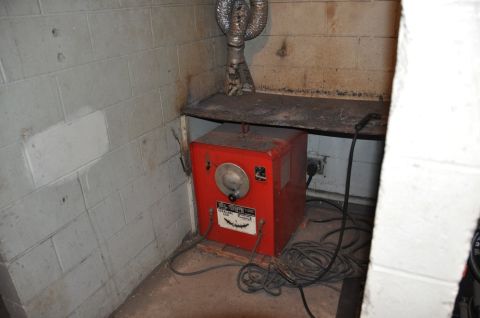 1996 Ford Bronco - A red welding machine sits on a concrete floor in a cinder block room.
