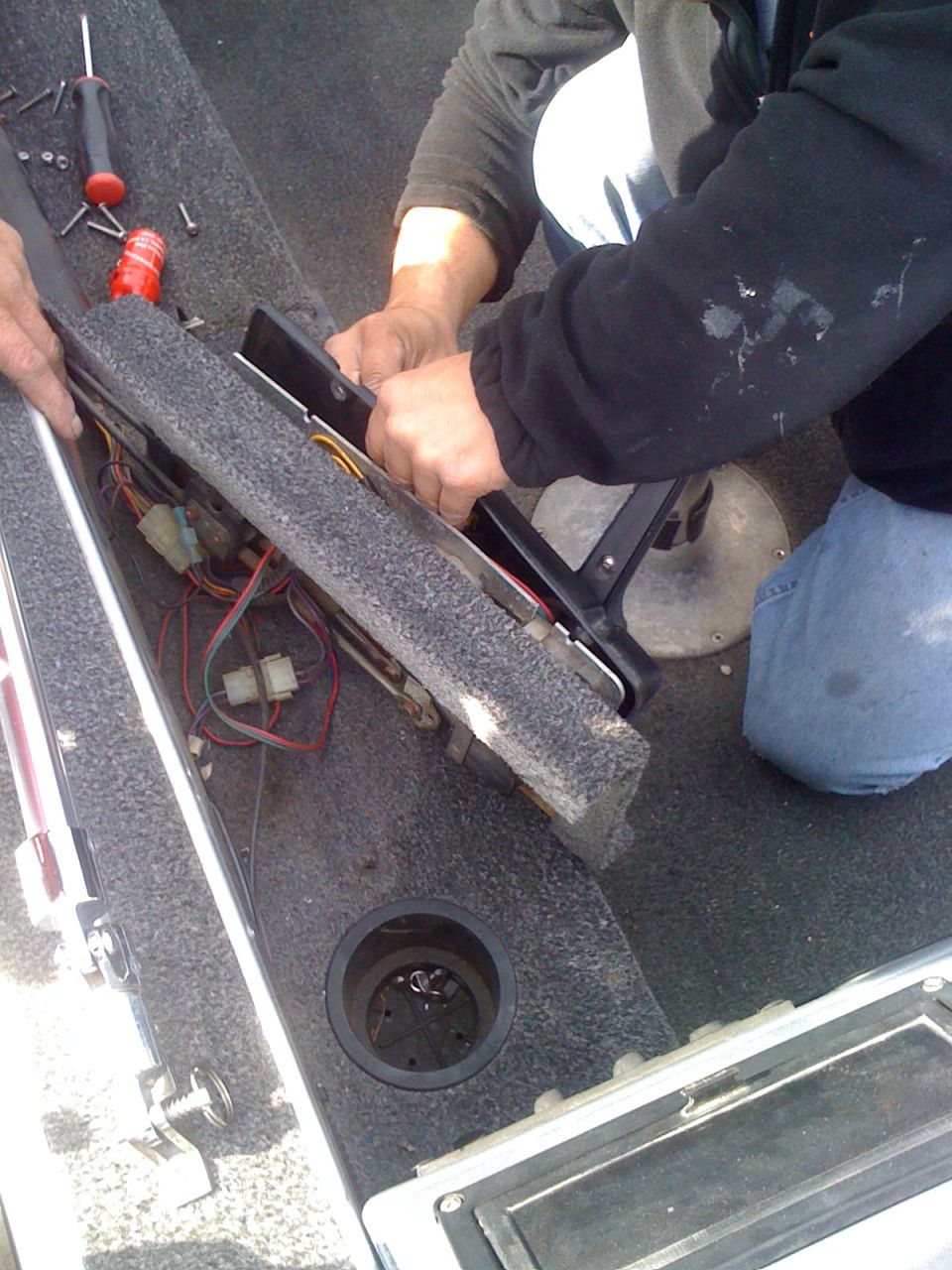 Boat interior with exposed wiring, cup holder, and people working on a console