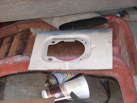 1973 Ford Ranchero - A metal plate with a circular cutout and mounting holes is placed on a red plastic vehicle body panel, with a spray can and cup nearby.