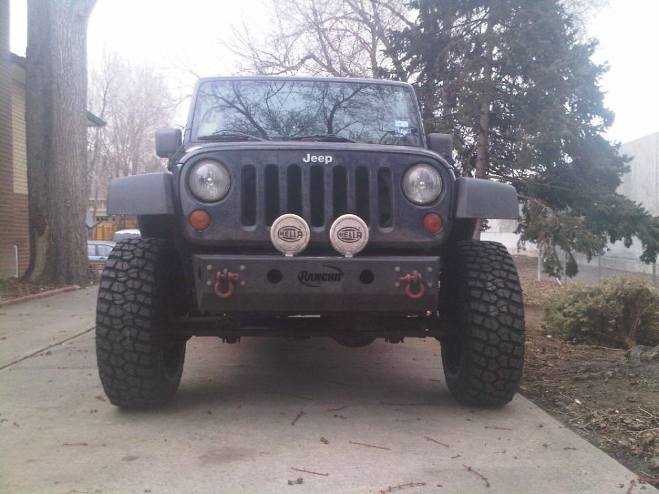 Lifted dark gray Jeep Wrangler JK front view with Rancho bumper, red shackles, and Hella lights