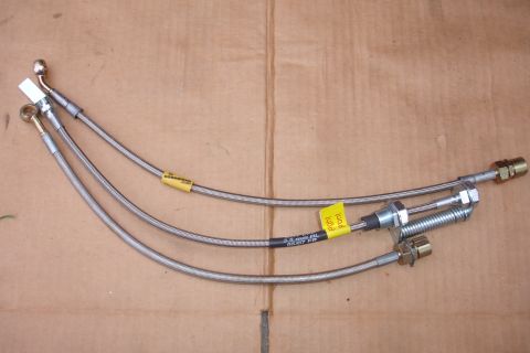 1995 Ford Taurus - Three stainless steel brake lines are laid out on a brown surface, with yellow tags indicating their application.