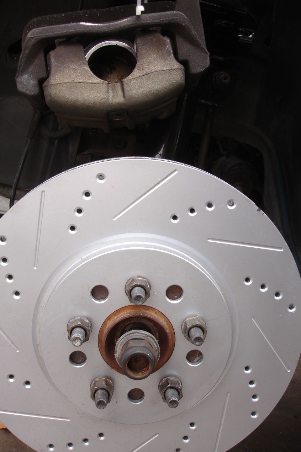 Brake caliper over a drilled and slotted rotor with five lug nuts visible