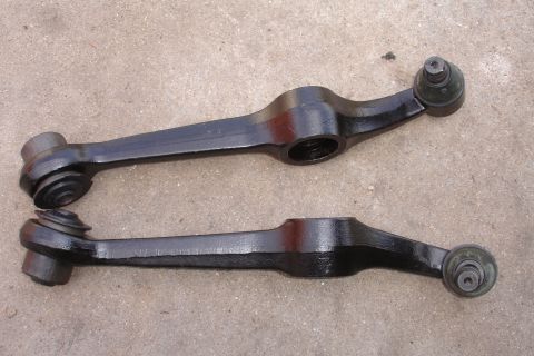 1995 Ford Taurus - Two black control arms, likely for a vehicle's suspension system, are displayed on a concrete surface.