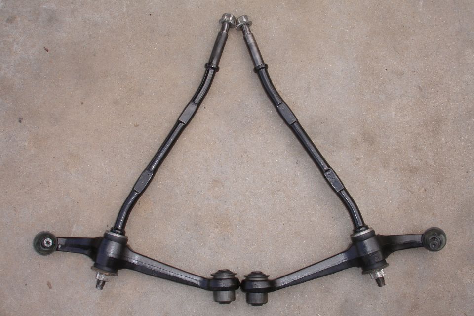 Pair of black front lower control arms and tie rods laid out on concrete