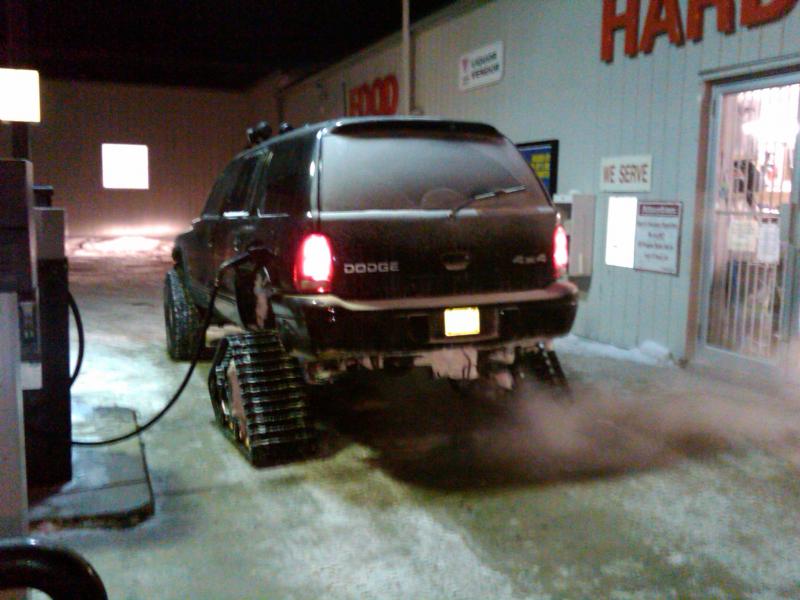 Black Dodge SUV on track conversion at a gas pump at night