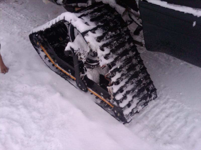 Snow-covered rubber track conversion with orange suspension arm and front ski on snow