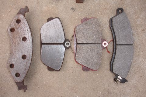 1995 Ford Taurus - A collection of brake pads, some new and some worn, are laid out on a concrete surface.