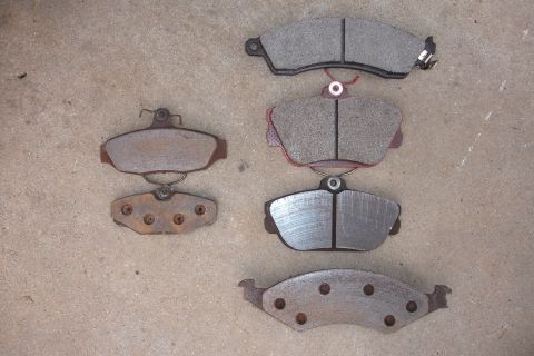 1995 Ford Taurus - A collection of various brake pads are displayed on a textured concrete background.