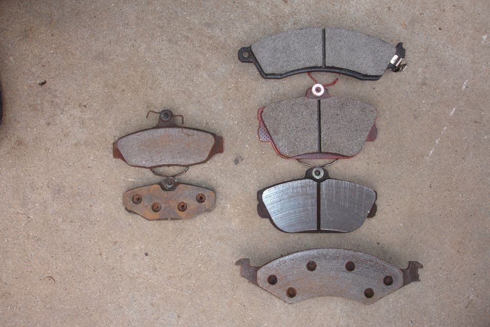 Several sets of brake pads laid out on a concrete surface. Some are new, others show wear and rust