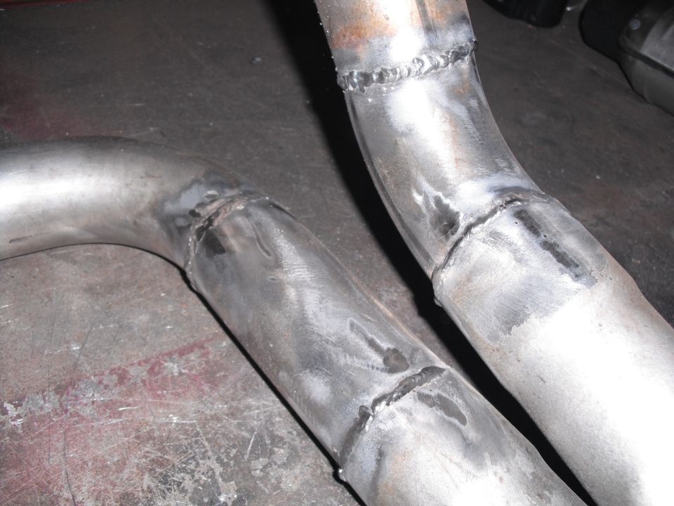 Two welded metal exhaust pipes on a workshop floor