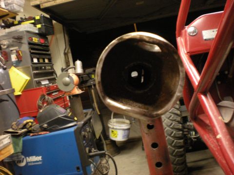 2009 Suzuki Samurai - A close-up view of an exhaust pipe, with a red roll cage and tire in the background, alongside workshop equipment.
