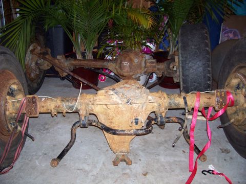 1994 Ford Bronco - Front and rear axles with wheels, showing significant rust and some red strapping.