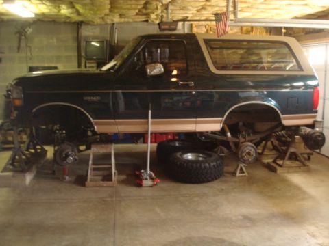 1995 Ford Bronco - A dark green Ford Bronco is elevated on jack stands in a garage, with its wheels off for maintenance.