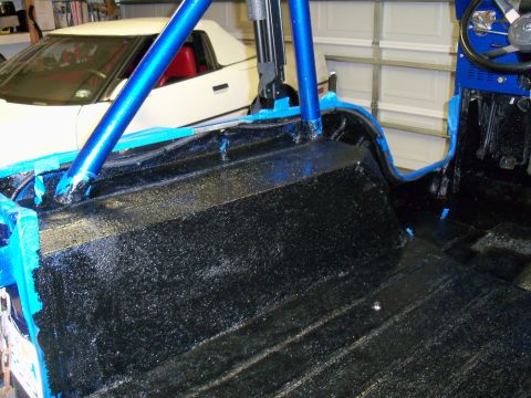1978 Jeep CJ5 - The interior of a Jeep shows a black textured floor and blue roll cage, with a white convertible visible behind it.