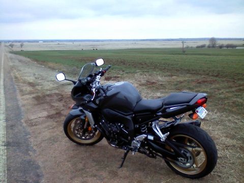 2008 Yamaha FZR1000 - A motorcycle is parked on the side of a road with a vast, open field in the background under a cloudy sky.