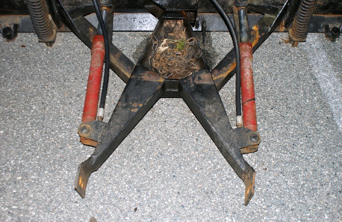 Black snow plow attachment with red hydraulic cylinders and a bird's nest in the center
