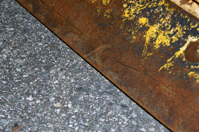 Rusted metal edge with yellow paint flecks over asphalt