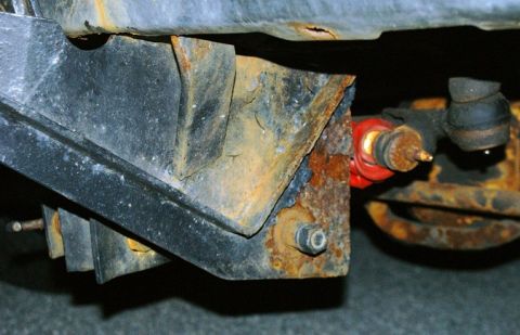 1979 Ford Bronco - Close-up view of heavily rusted frame brackets and suspension components on a vehicle's undercarriage.