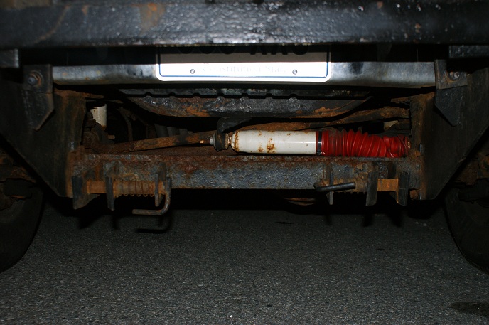 Undercarriage view showing rusty frame, suspension components, and a license plate