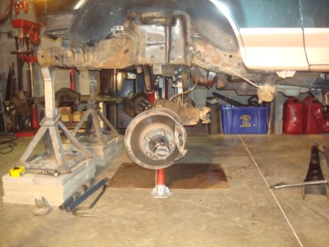1995 Ford Bronco - The frame and suspension components of a vehicle are visible while it is supported by jack stands in a garage setting.