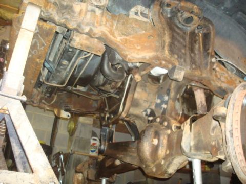 1995 Ford Bronco - The heavily rusted undercarriage of a vehicle is shown, with suspension and drivetrain components visible.