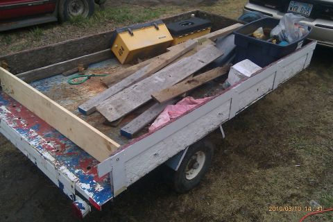 2000 Mercury Grand Marquis - A utility trailer is filled with lumber and various items, parked next to two cars.
