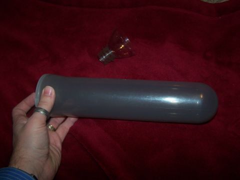 1986 Ford Bronco - A hand holds a gray cylindrical object with a glass bulb nearby against a red fabric background.