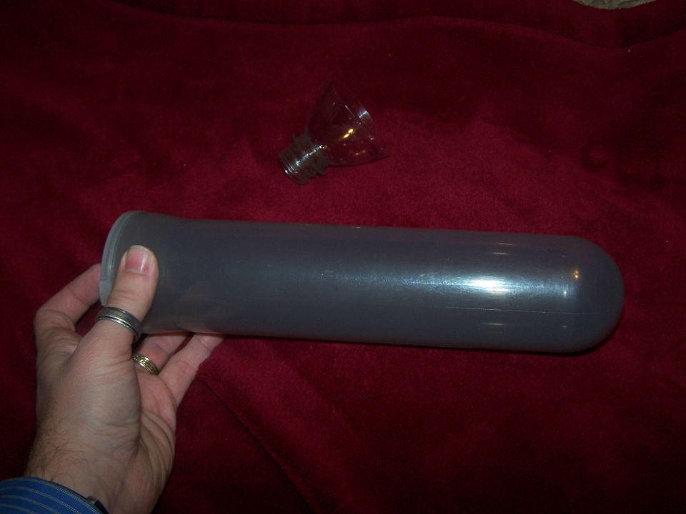 Gray plastic cylinder held by a hand with rings, next to a glass bulb on a red cloth