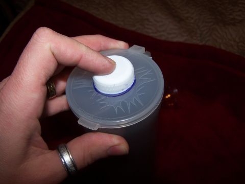 1986 Ford Bronco - A hand is shown holding a plastic cap with a white screw-on lid, with a blue ring visible underneath.