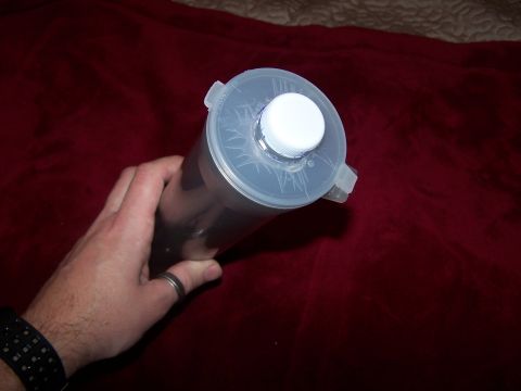 1986 Ford Bronco - A hand holds a clear plastic container with a white cap against a red fabric surface.