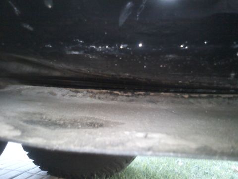 1986 Ford Bronco - Close-up view of a vehicle's undercarriage, revealing dirt accumulation and a tire.
