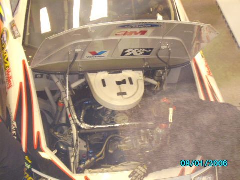 1978 Ford Bronco - The engine bay of a race car is visible with the hood open, revealing the engine and numerous sponsor decals.