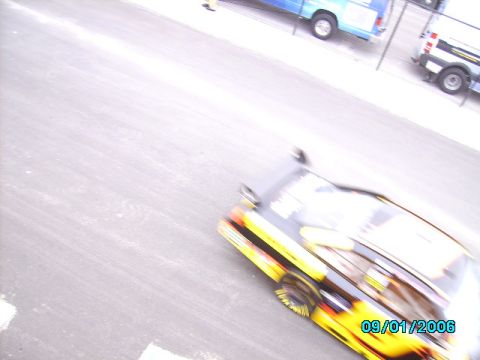 1978 Ford Bronco - A race car with flame decals is captured in motion on a track, with other vehicles visible in the background.