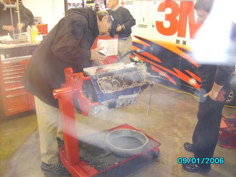 1978 Ford Bronco - Mechanics work on an engine block in a garage setting, with a large 3M branded trailer in the background.