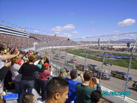 1978 Ford Bronco - Spectators fill the stands at a NASCAR race, with cars speeding around the track under a clear blue sky.