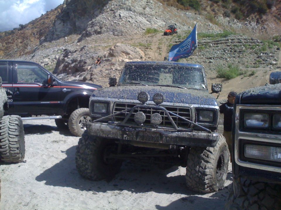 Muddy 1979 Ford Bronco with custom bumper and off-road tires, parked next to another truck