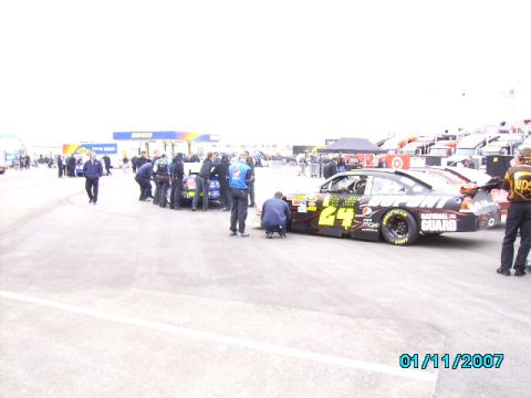 1978 Ford Bronco - Race cars and crew members are gathered in the pit area with a gas station in the background.