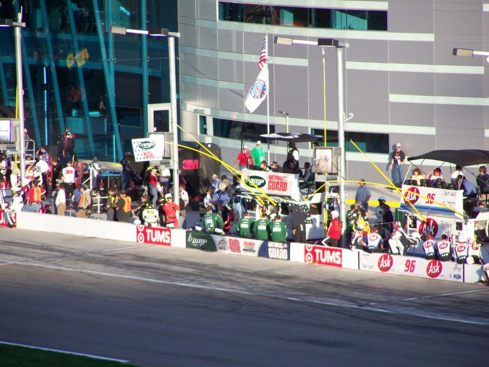 NASCAR pit crew and officials gathered on a race track with a building in the background