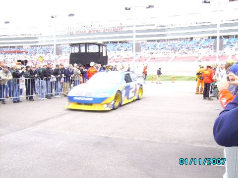 1978 Ford Bronco - A race car speeds past a crowd of onlookers at a motor speedway.